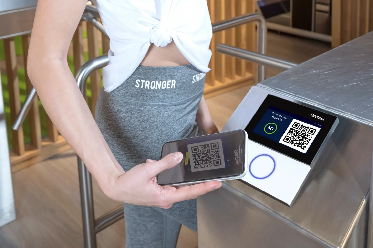 A member scans a QR code to enter the gym through a Gantner turnstile.