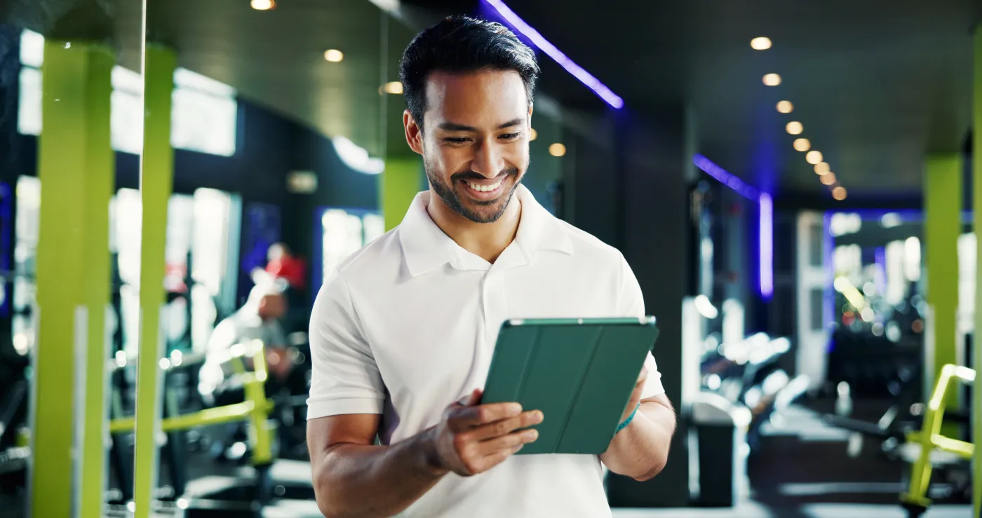 A trainer smiles while checking the studio's system on a tablet on the gym floor